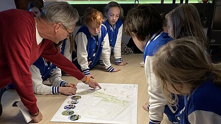 De kindergemeenteraad bekijkt een plattegrond en krijgt uitleg over de inrichting van een speeltuin