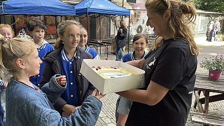 Kinderen van de kindergemeenteraad geven een grote slagroomtaart aan een medewerker van de kinderboerderij.