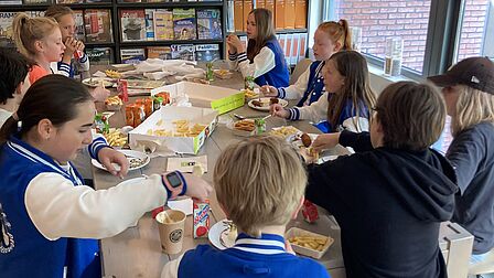 De kinderen van de kindergemeenteraad eten patat aan tafel met elkaar