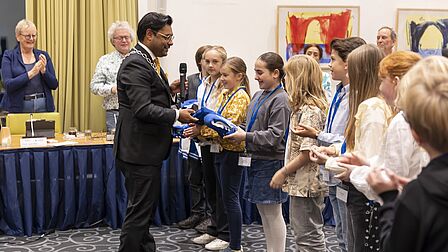 Burgemeester Falgun Binnendijk deelt een speciale jas uit aan de kinderen van de kindergemeenteraad.